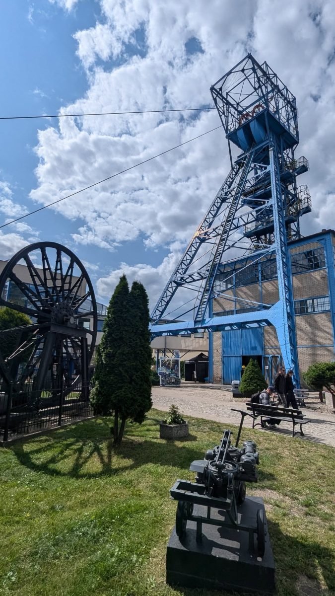 Niebieska wieża szybowa kopalni Guido w Zabrzu i dawne maszyny górnicze na trawniku