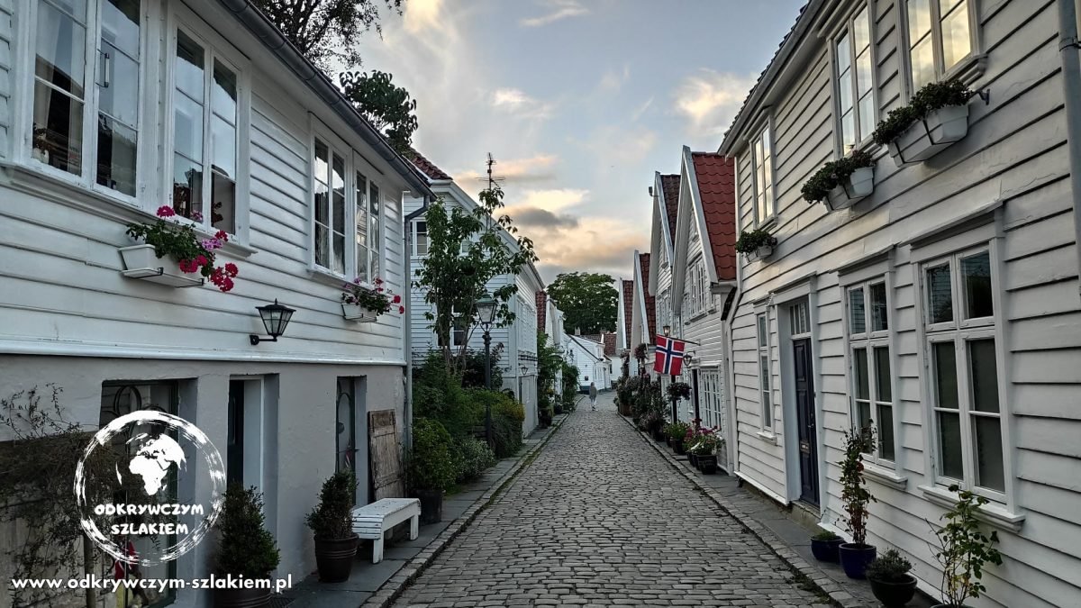 Brukowana uliczka z białymi drewnianymi domkami w Gamle Stavanger w słońcu