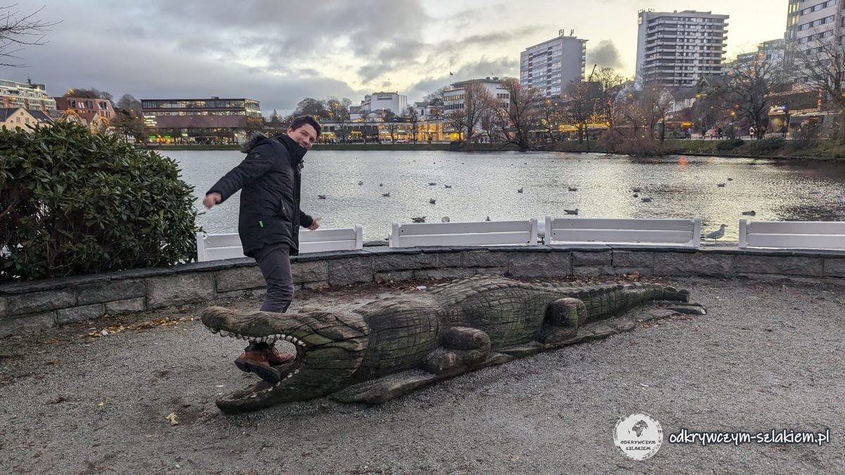 Zabawa przy drewnianej rzeźbie krokodyla nad jeziorem w centrum Stavanger