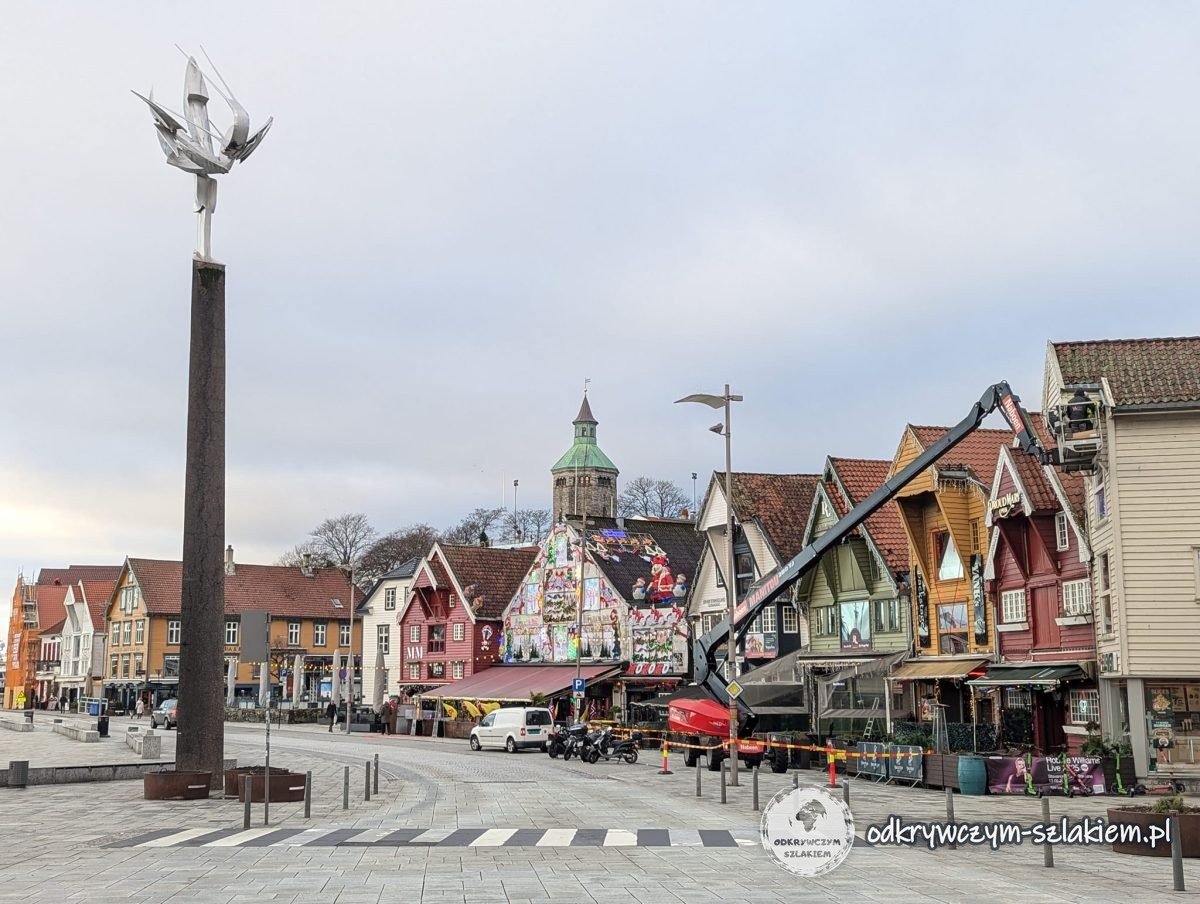 Plac nad portem Vågen z rzeźbą na wysokim słupie i kolorowymi domami w tle