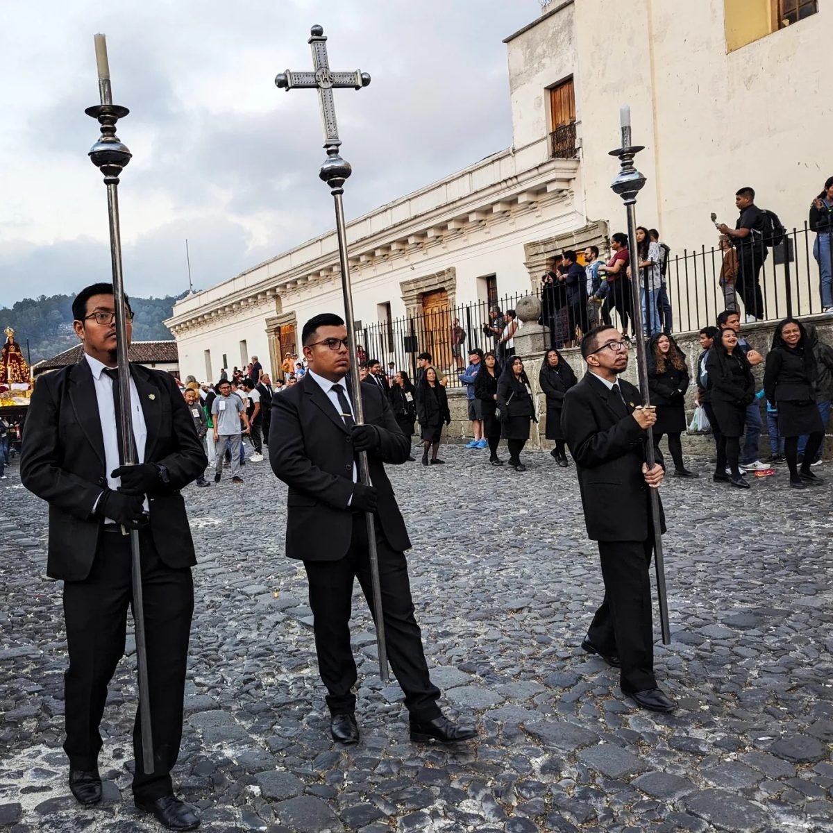Mężczyźni w czarnych garniturach niosący krzyże na czele procesji w Antigua Guatemala