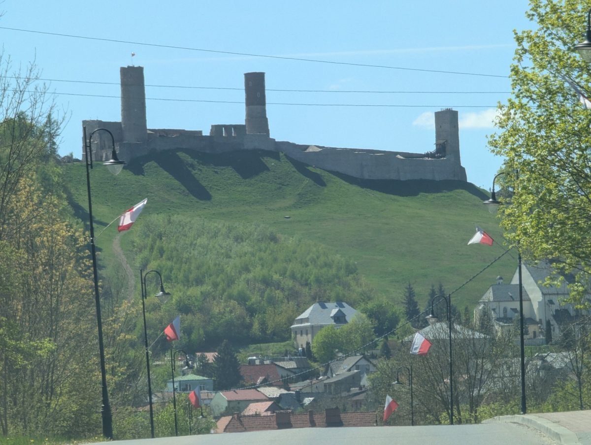 Ruiny zamku w Chęcinach na zielonym wzgórzu nad miastem, przy drodze biało-czerwone flagi