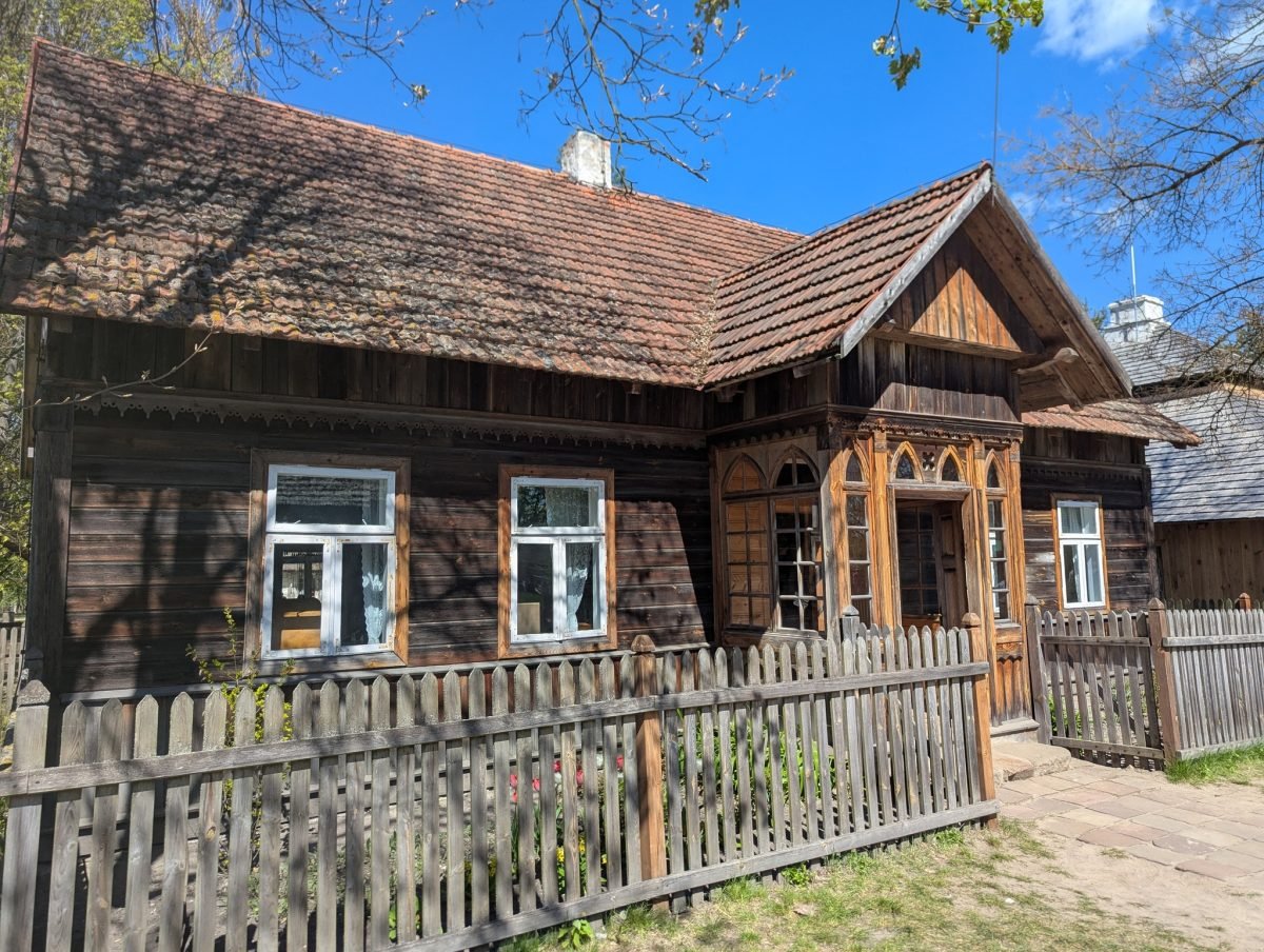 Drewniany dom z gankiem i sztachetowym płotem w skansenie w Tokarni