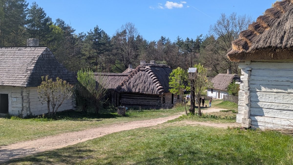 Bielone chaty kryte strzechą przy polnej drodze w skansenie w Tokarni