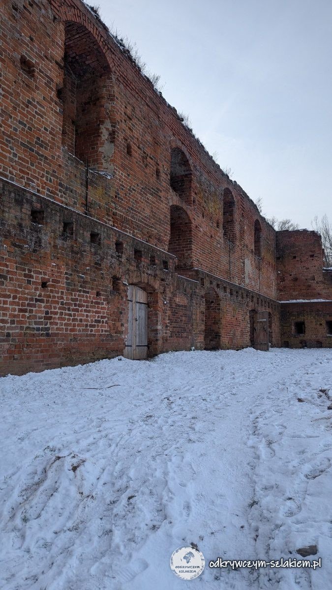 Alta muralla de ladrillo del castillo de Dybów sobre el patio nevado