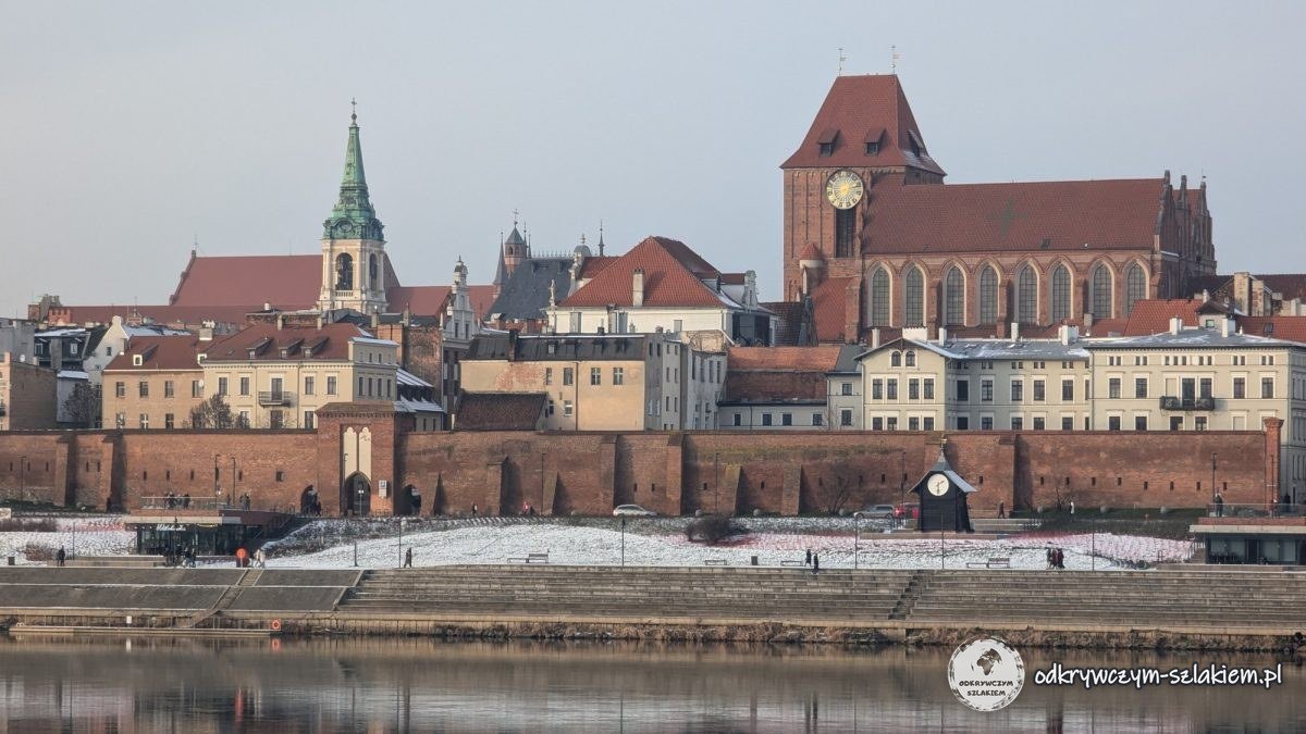Panorámica del casco antiguo de Toruń desde la orilla izquierda del Vístula: la catedral de los Santos Juanes, el Ayuntamiento y las murallas reflejados en el agua en calma