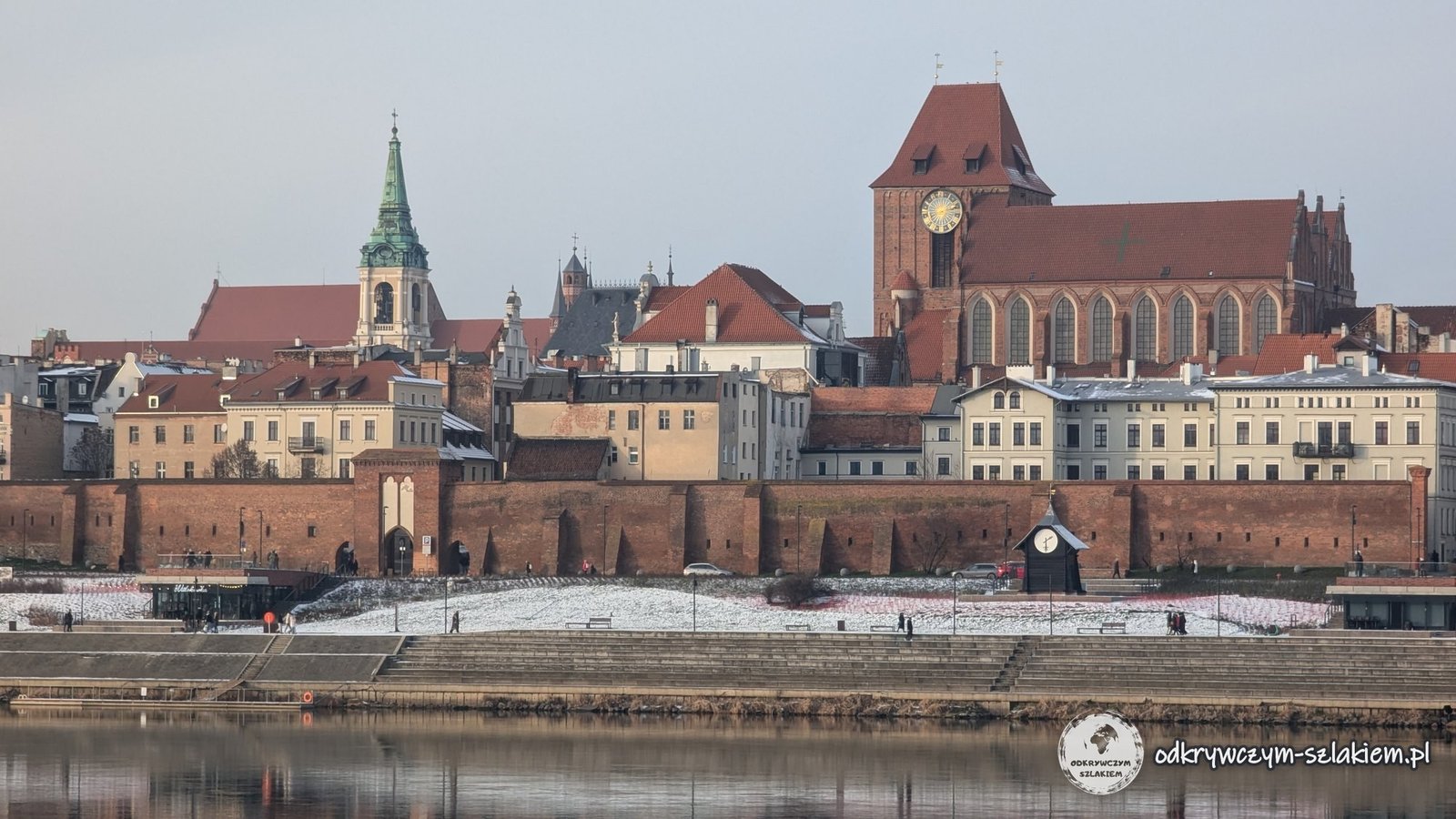 Panorámica del casco antiguo de Toruń desde la orilla izquierda del Vístula: la catedral de los Santos Juanes, el Ayuntamiento y las murallas reflejados en el agua en calma