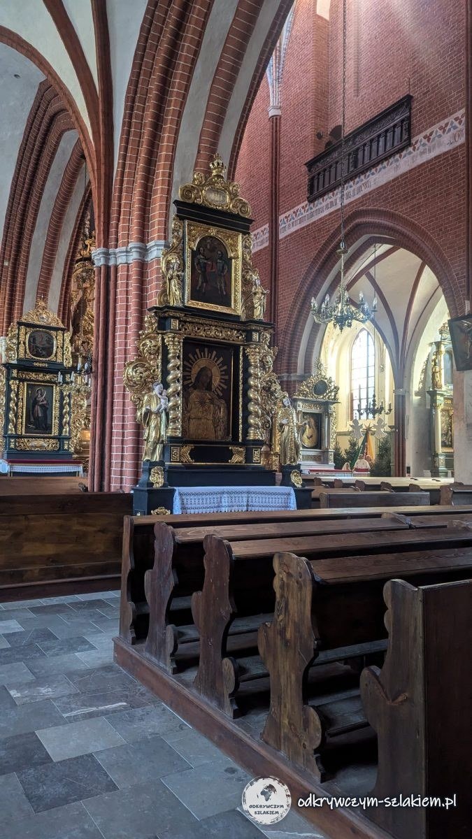 Interior de la iglesia de Santiago de Toruń con bóvedas de ladrillo, bancos y un altar