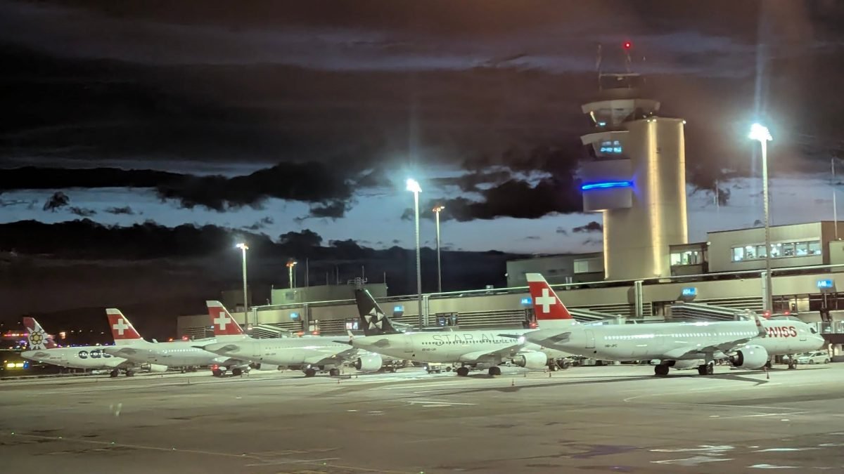 Samoloty Swiss na płycie nocnego lotniska w Zurychu, w tle wieża kontroli lotów