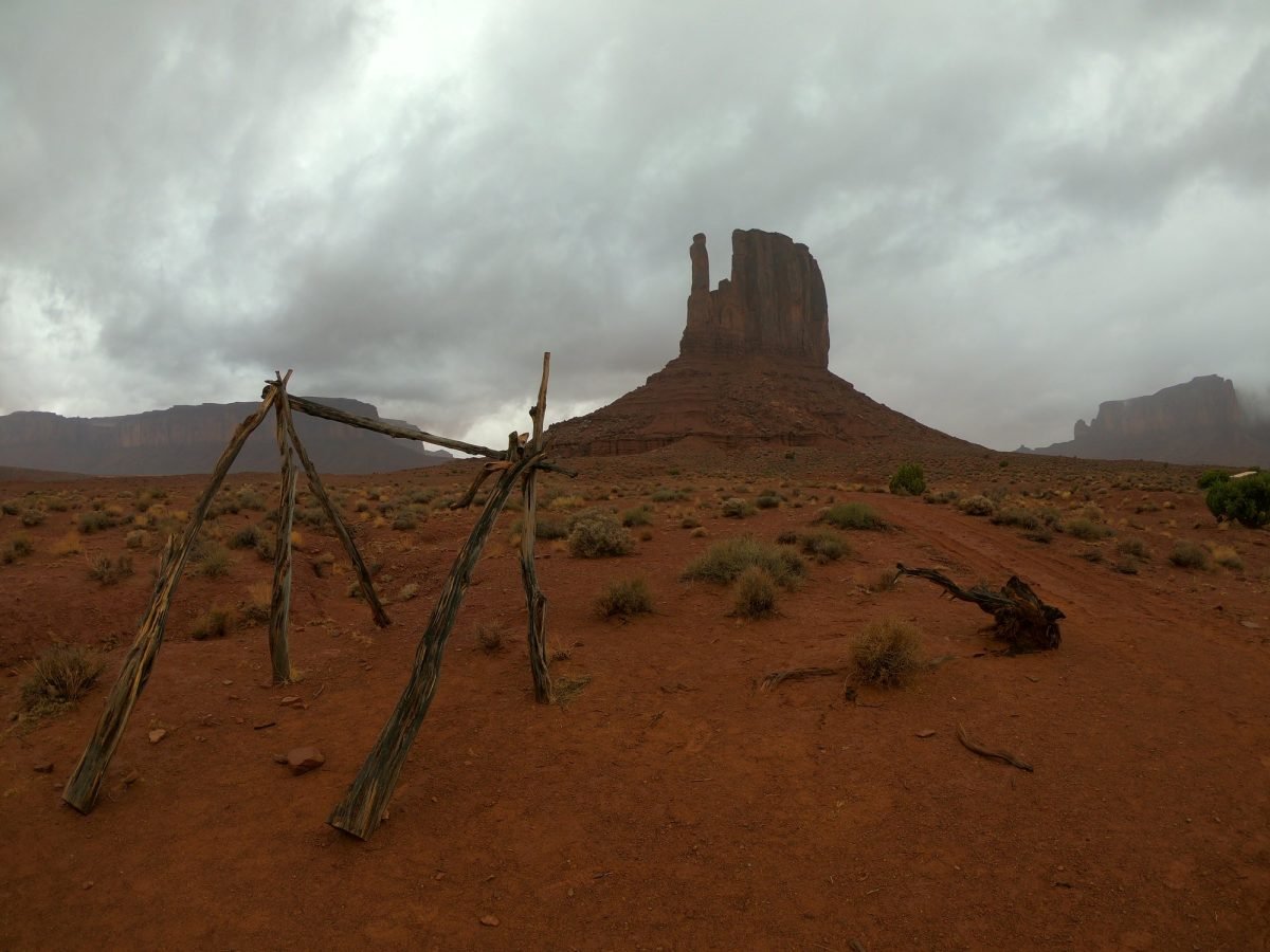 Drewniana konstrukcja z żerdzi na tle ostańców Mitten w Monument Valley