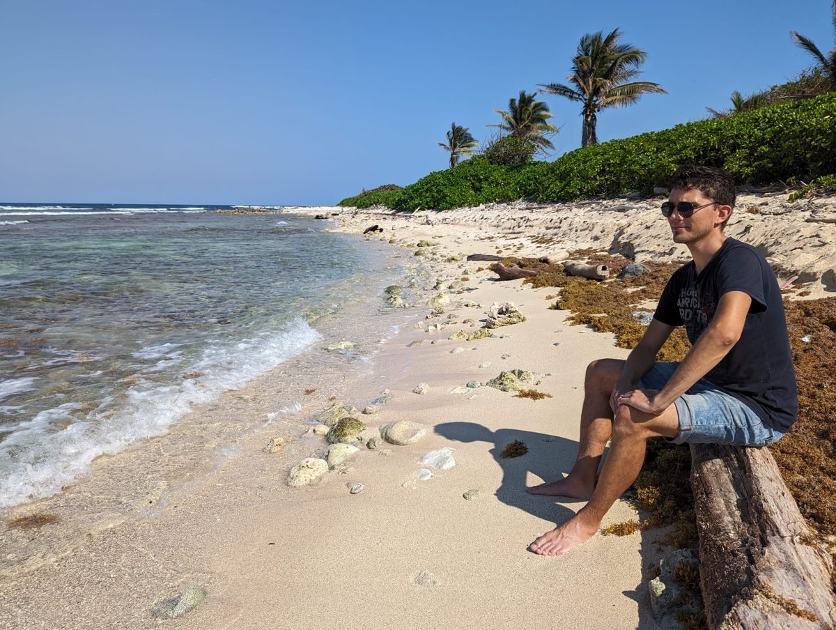 Maciek na kłodzie na dzikiej plaży z rafą przy brzegu, Utila
