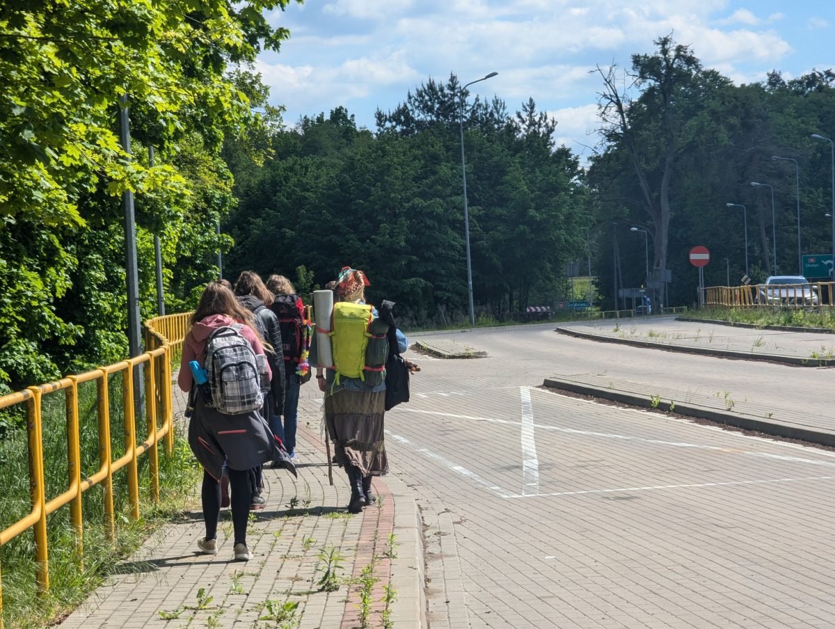 Uczestnicy z plecakami idą chodnikiem w Iławie w stronę mariny
