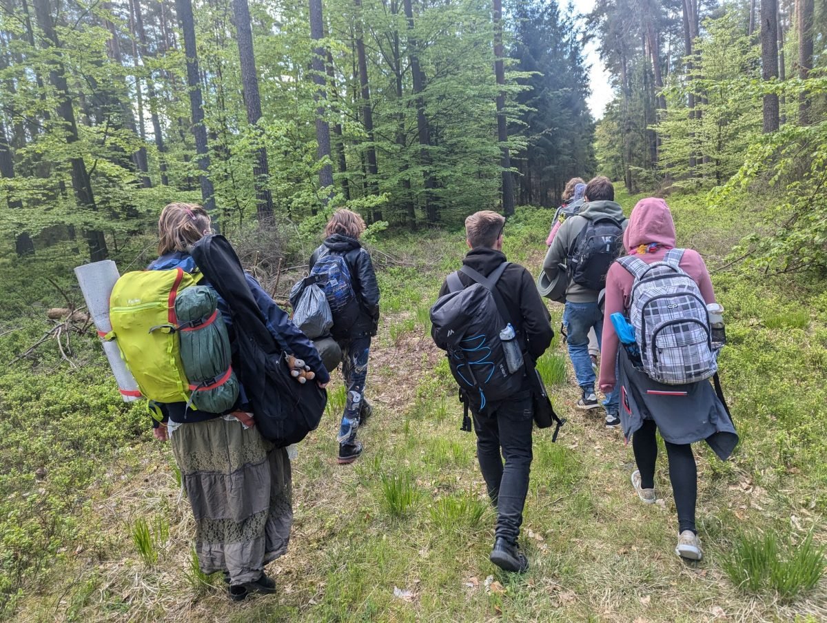 Uczestnicy z plecakami i karimatami idą przez las drugiego dnia