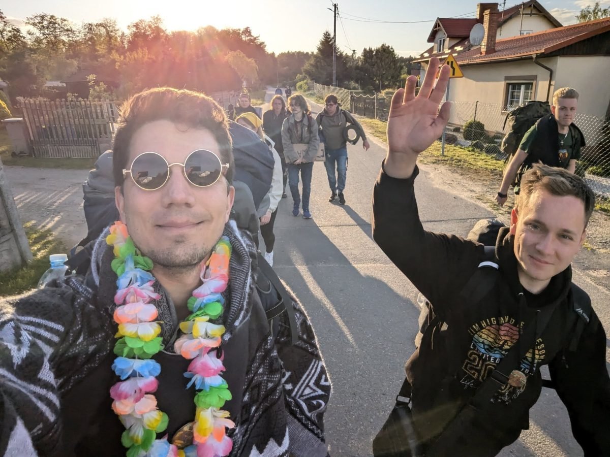 Maciek z uczestnikami marszu na wiejskiej drodze o zachodzie słońca
