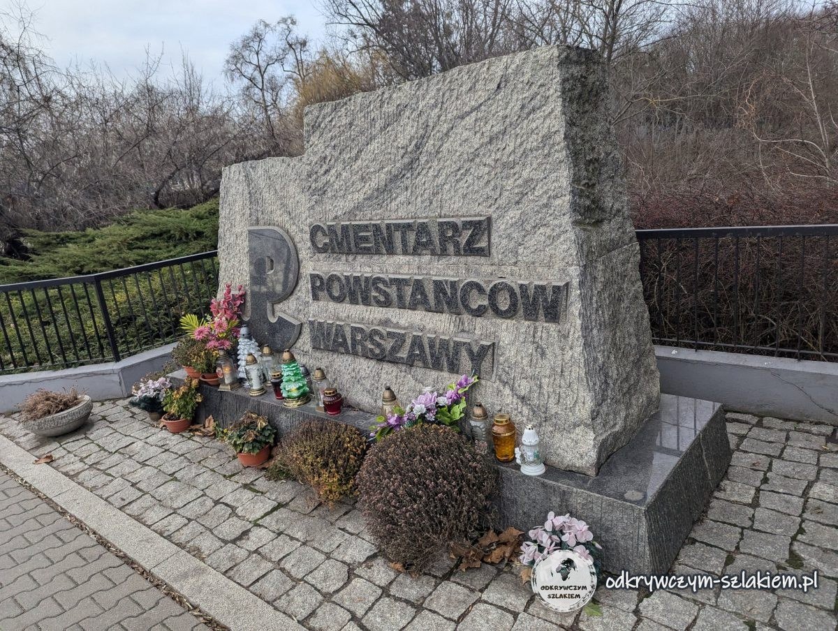 Una piedra con la inscripción Cementerio de los Insurgentes de Varsovia, con flores y velas en la entrada