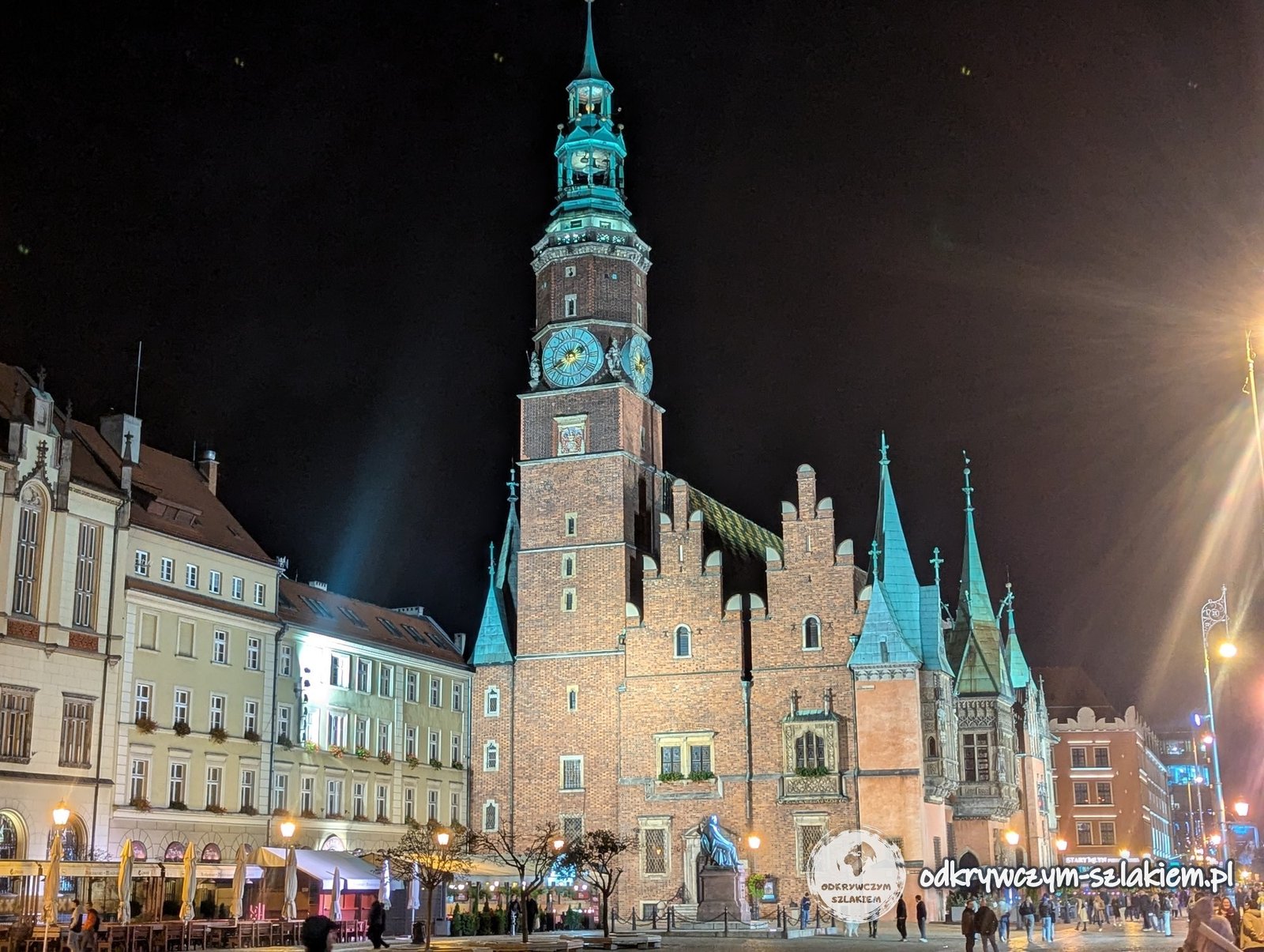 Gotycki Ratusz we Wrocławiu z wieżą i szczytami podświetlony nocą, przed nim mokra płyta Rynku