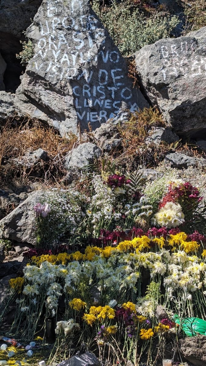 Kwiaty złożone pod skałą z wymalowanym napisem o Chrystusie na Cerro Quemado