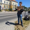 Maciek trampt mit einem Pappschild „Bisztynek“ an der Straße vor der Kreisverwaltung in Lidzbark Warmiński (Heilsberg)