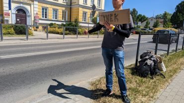 Maciek trampt mit einem Pappschild „Bisztynek“ an der Straße vor der Kreisverwaltung in Lidzbark Warmiński (Heilsberg)