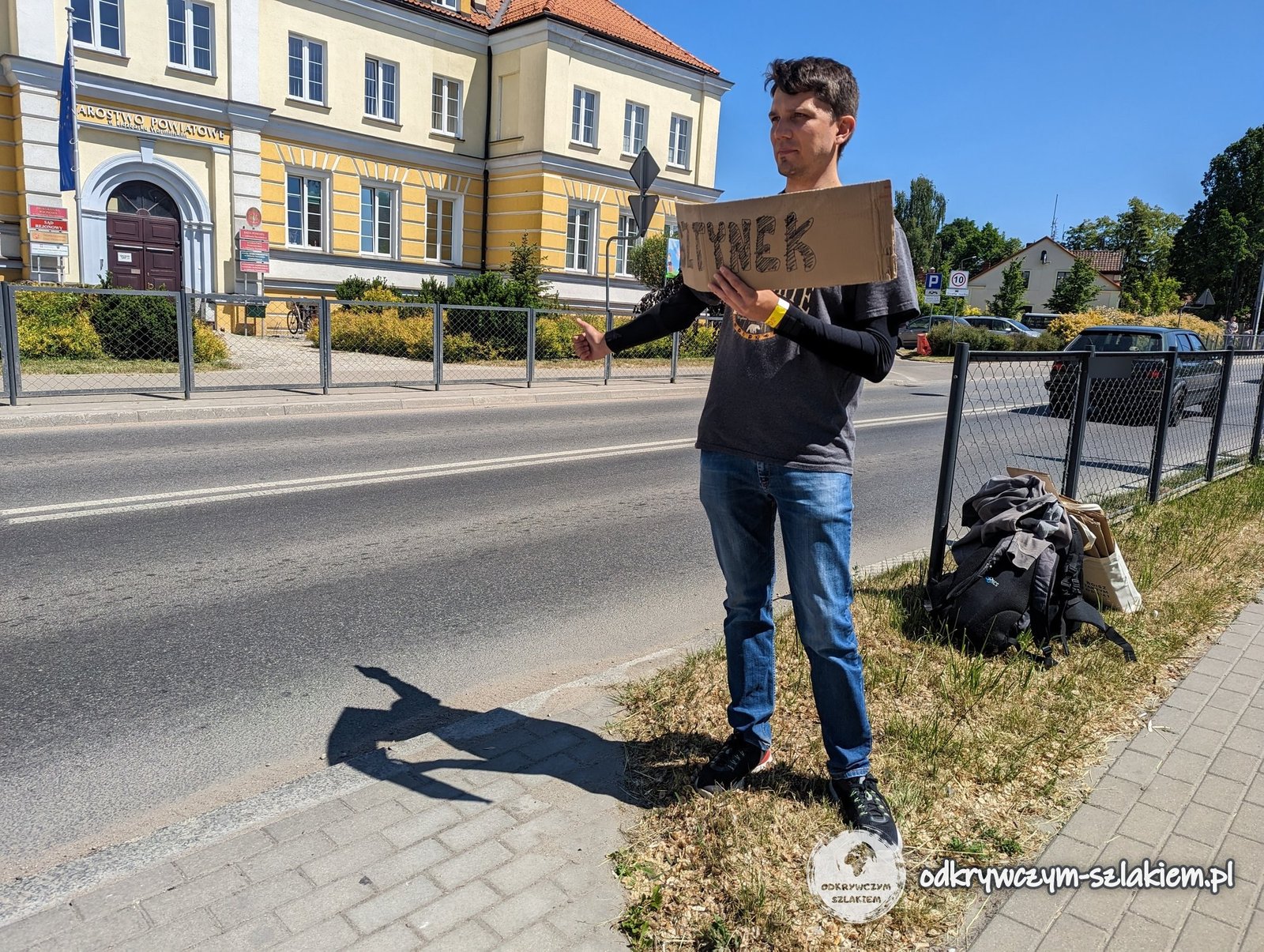 Maciek trampt mit einem Pappschild „Bisztynek“ an der Straße vor der Kreisverwaltung in Lidzbark Warmiński (Heilsberg)
