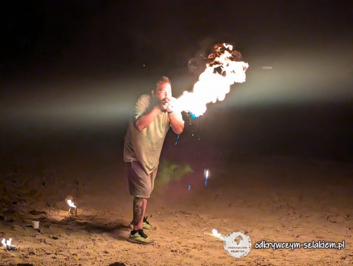 Ein Artist spuckt Feuer bei der nächtlichen Show auf dem sandigen Platz